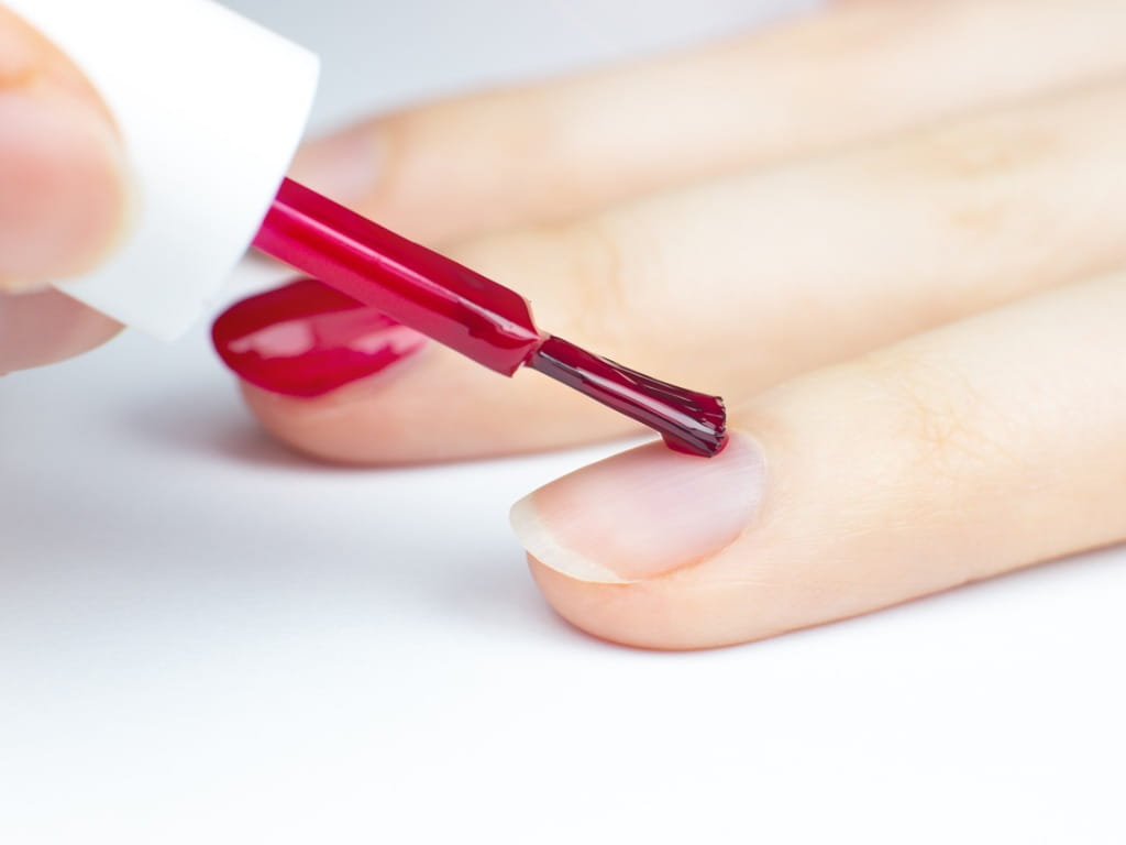 close up photo of nail red polish being painted on a woman's nails