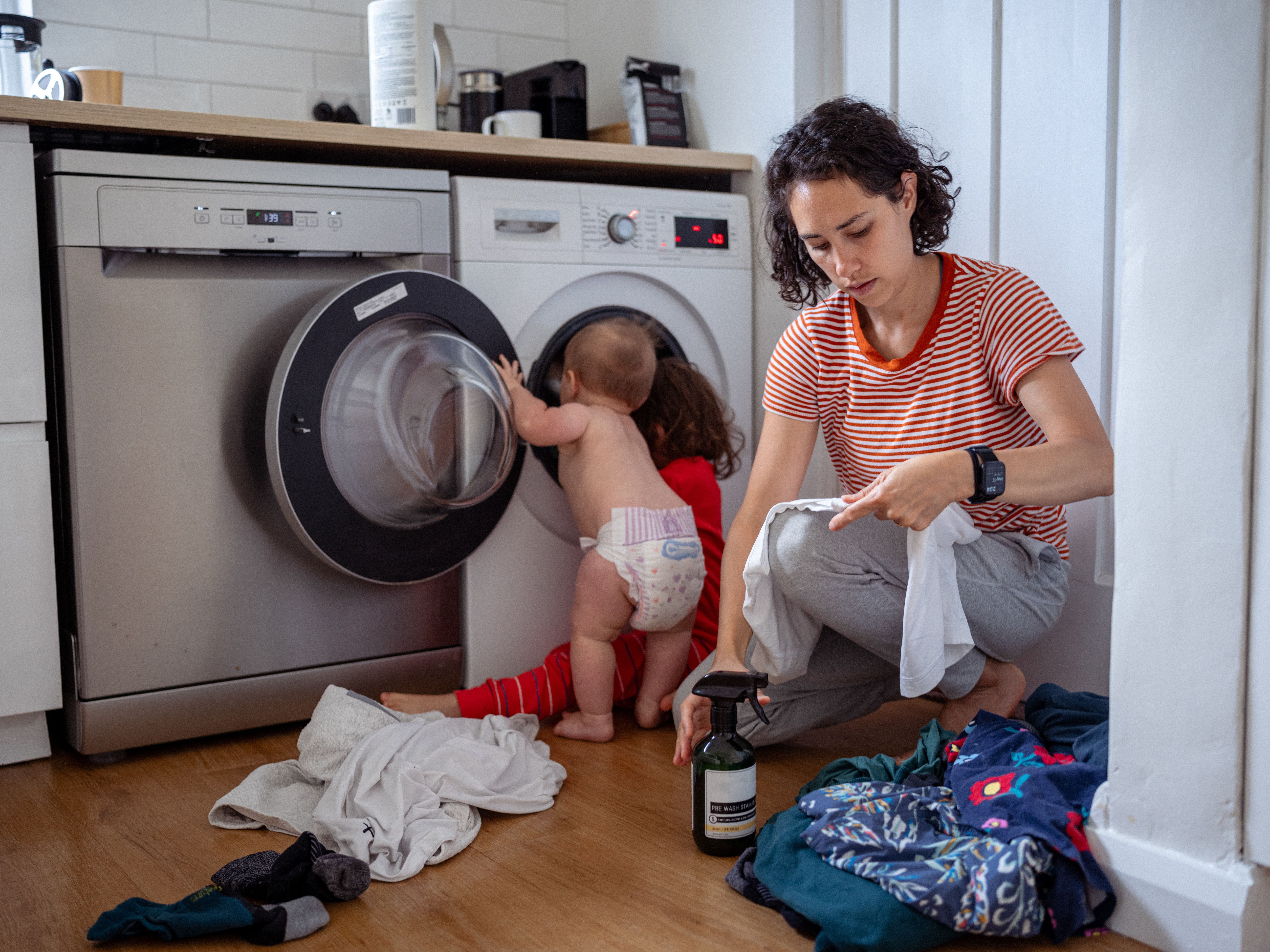child playing in washing machine as mother cleans clothes