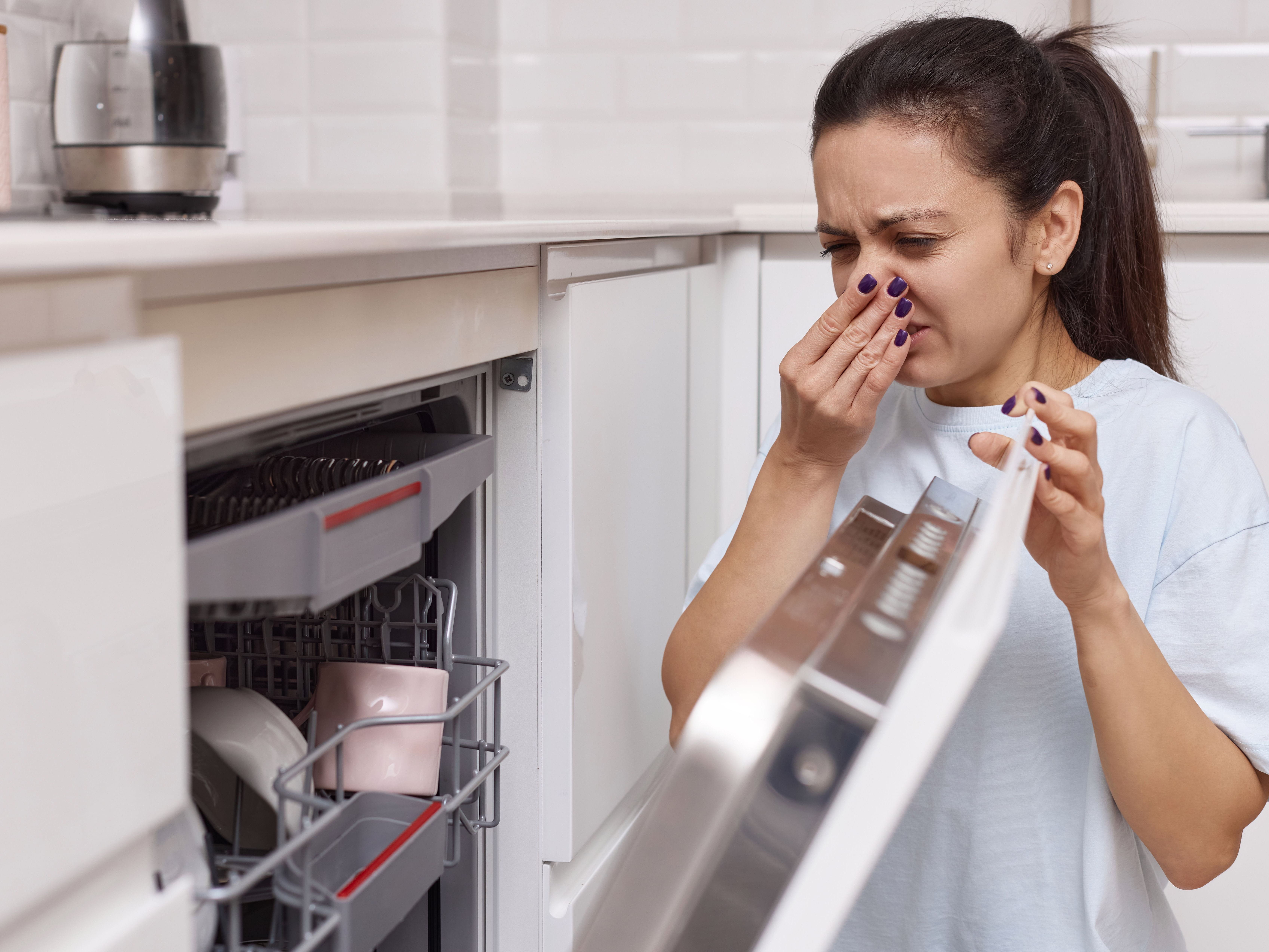 woman holding nose over dishwasher