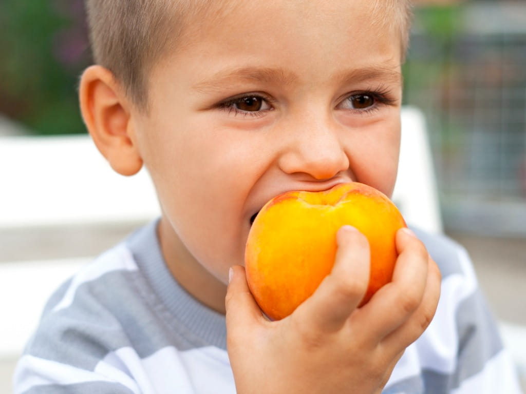 little boy eating a peach