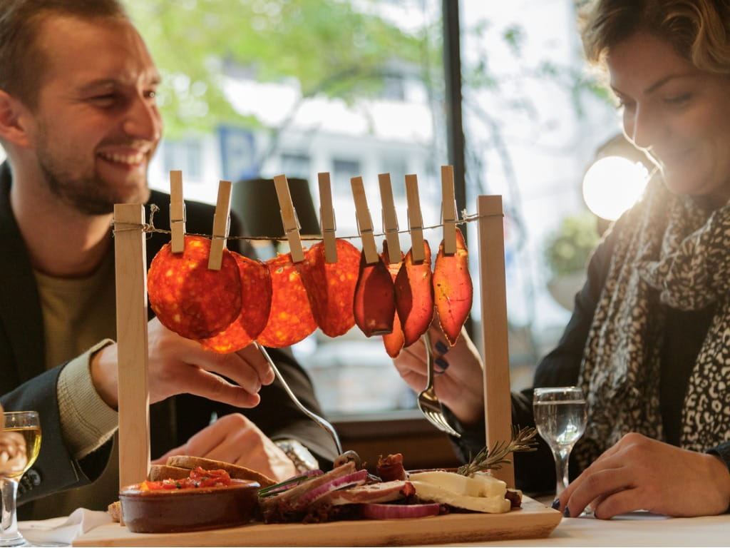 couple eating cured sausage hanging on a line