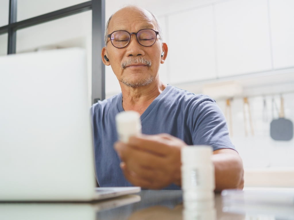 elderly man holding a medication bottle and checking his computer