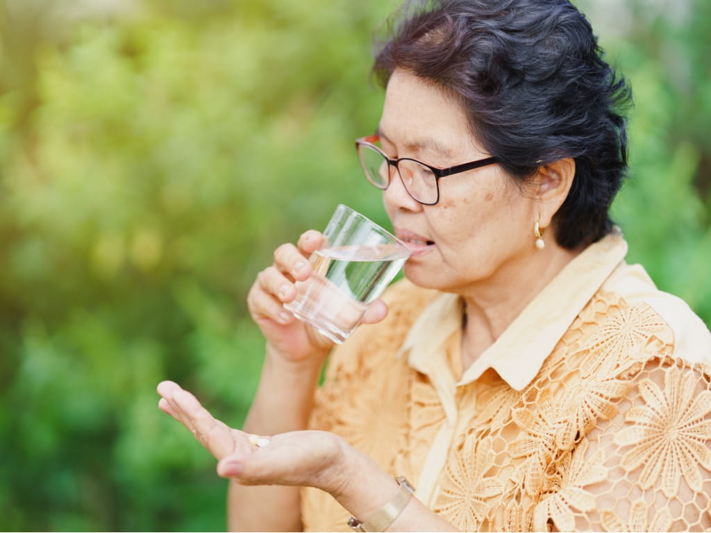 elderly woman holding a glass of water and pill