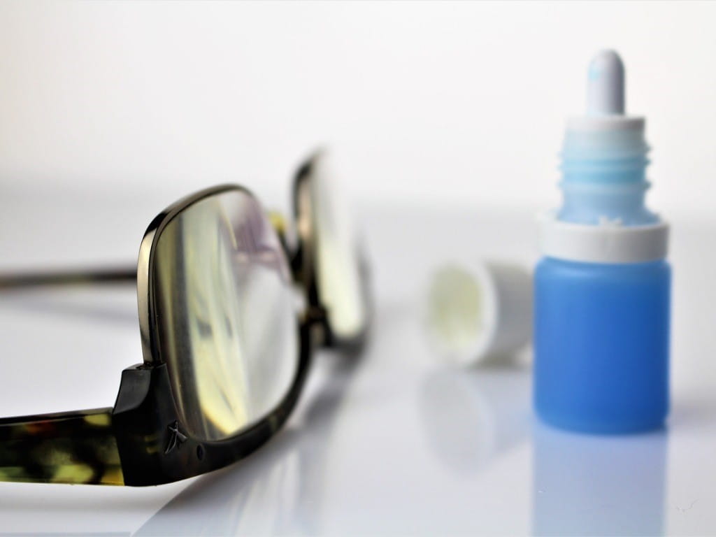 bottle of eye drops next to pair of glasses