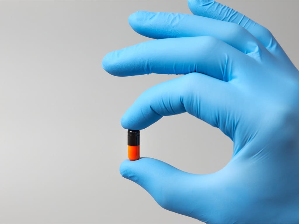 gloved hand holding orange and black pill