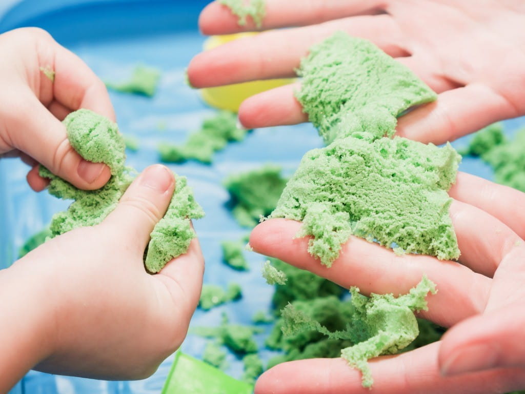 hands playing with green kinetic sand