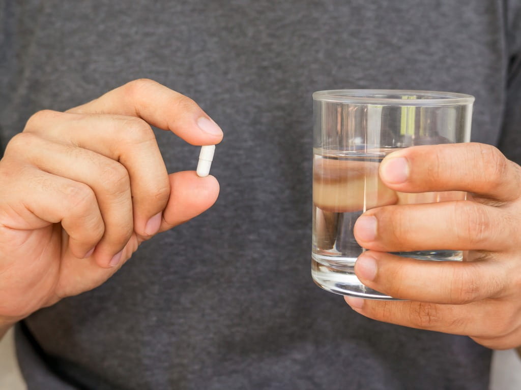 man holding a pill and a glass of water