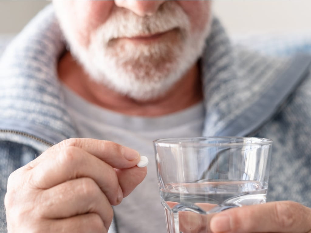 man holding a white pill and a glass of water