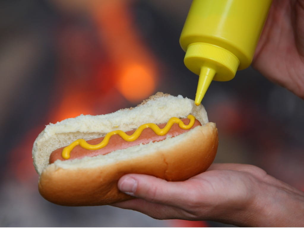 hand putting mustard on a hot dog