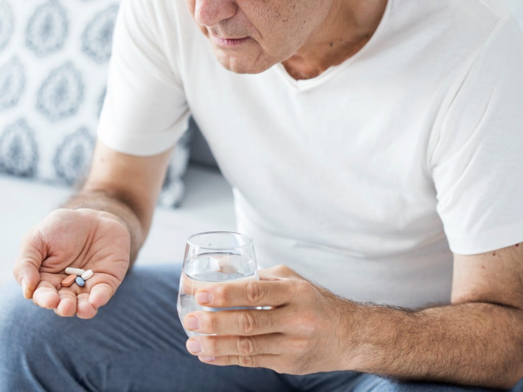 man holding medication in one hand and a glass of water in the other