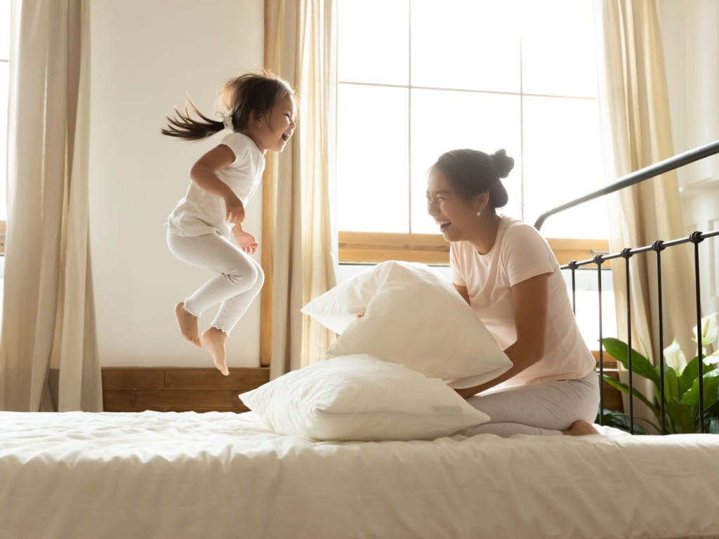 small child bouncing on bed next to mother