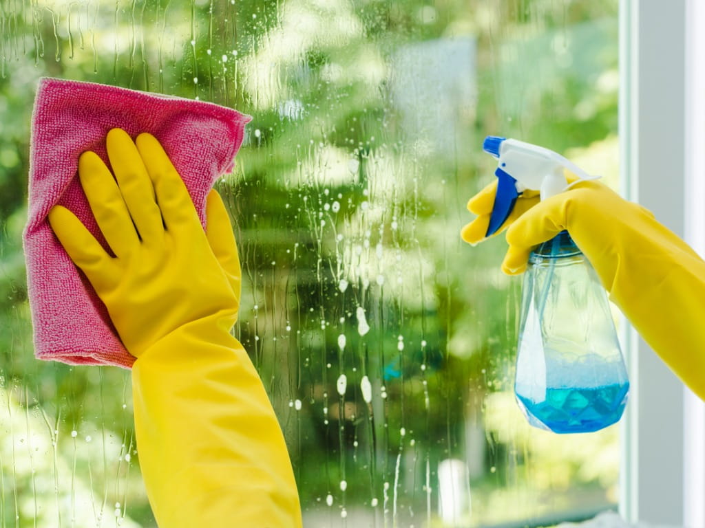 person spraying Windex bottle and wiping with a cloth