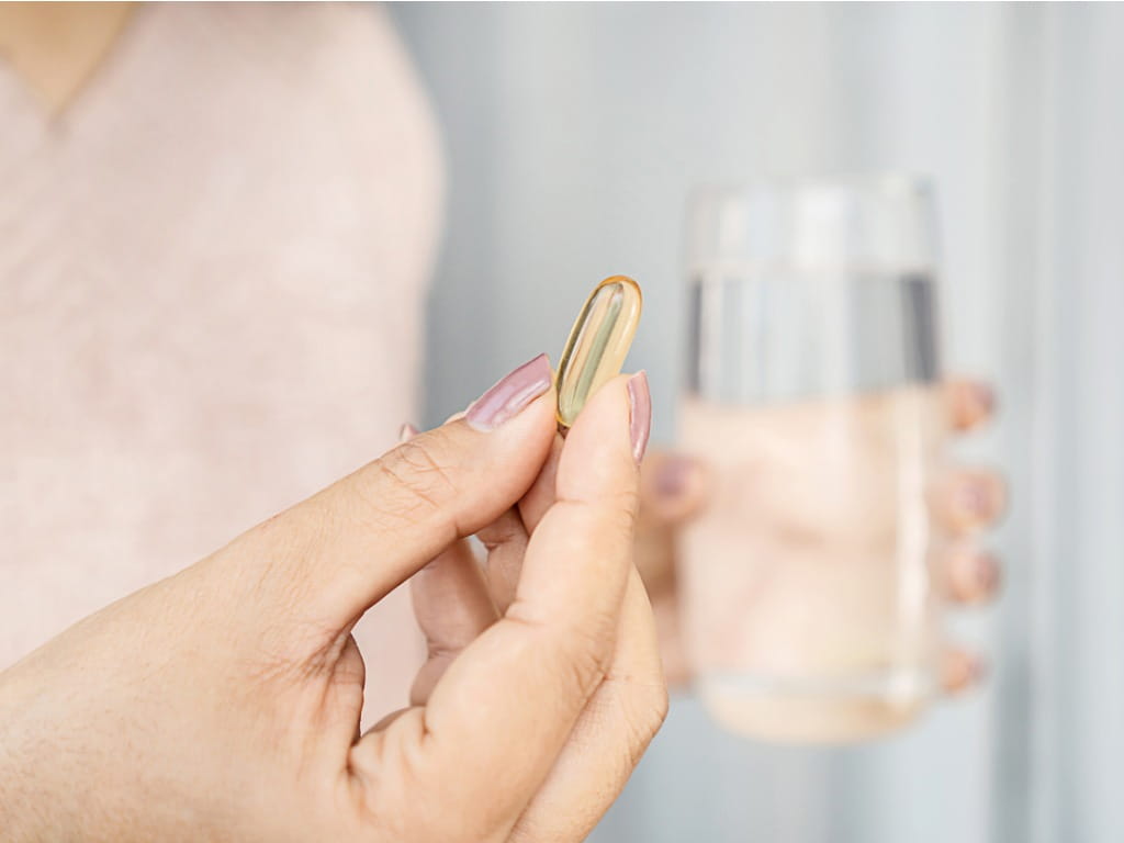 woman holding a capsule and glass of water