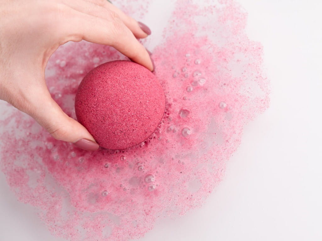 woman putting pink bath bomb in water