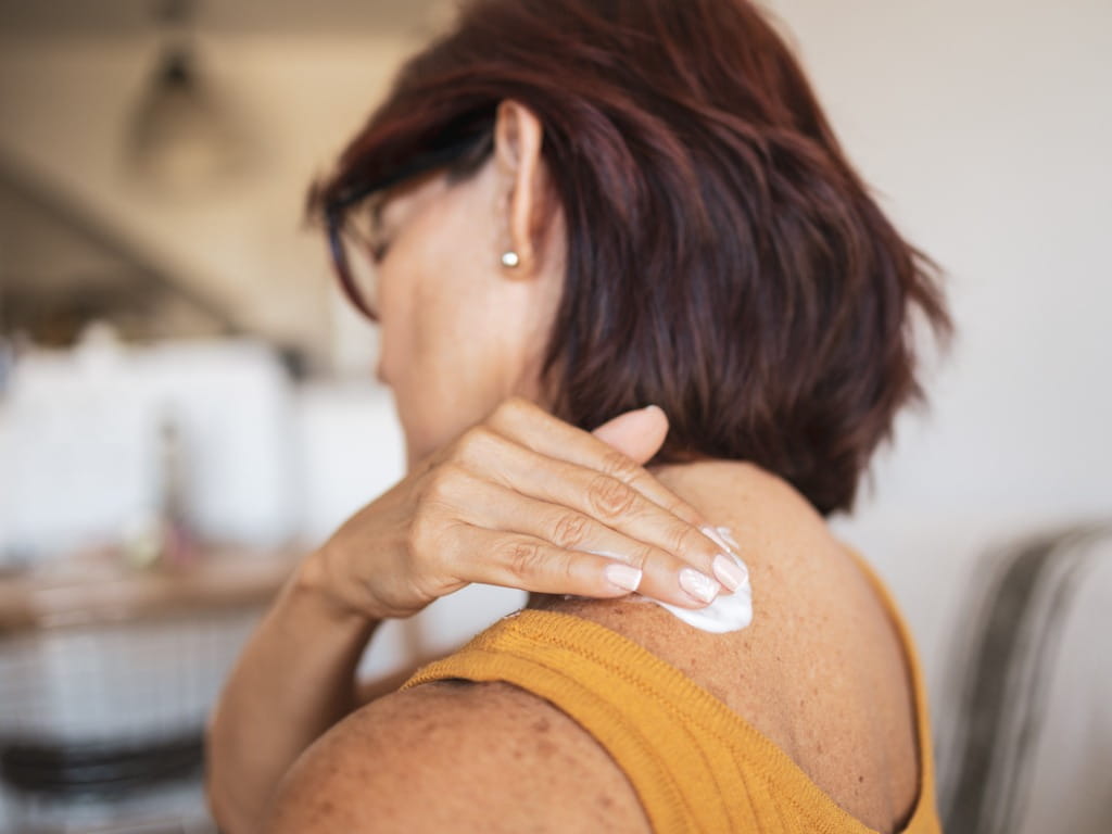 woman rubbing cream on her shoulder
