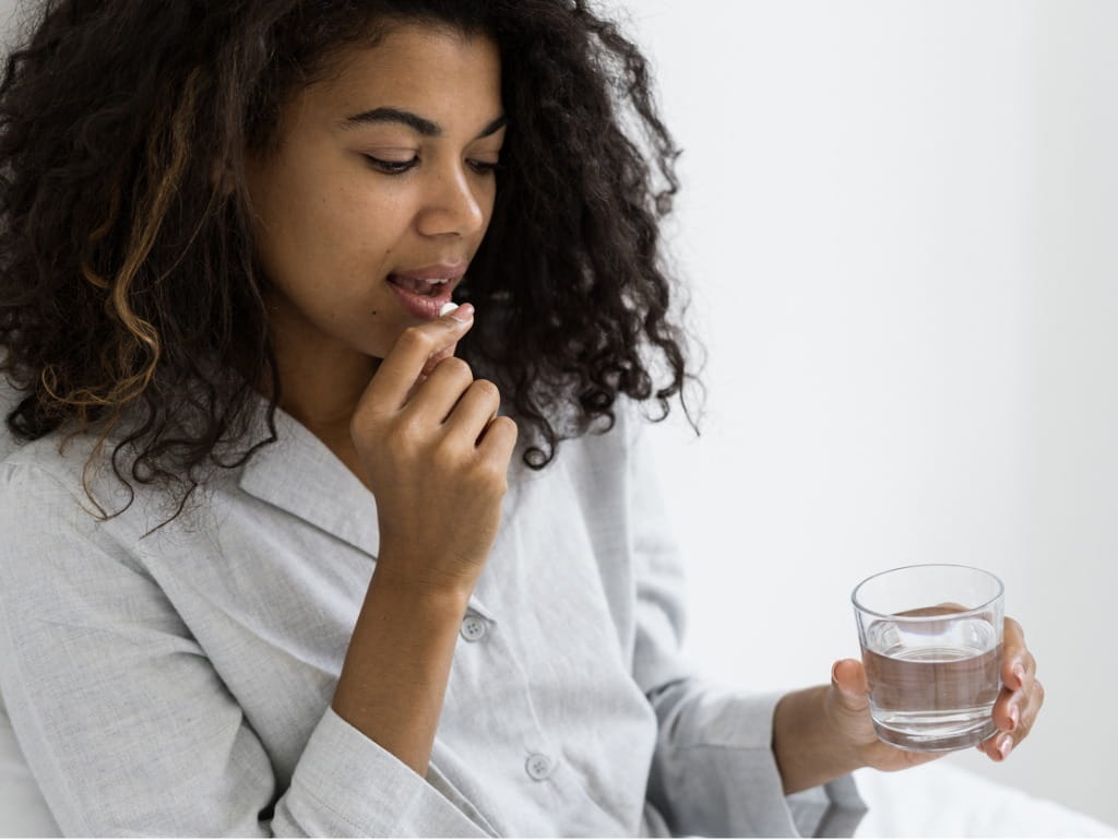 woman taking an amlodipine pill and holding a glass of water