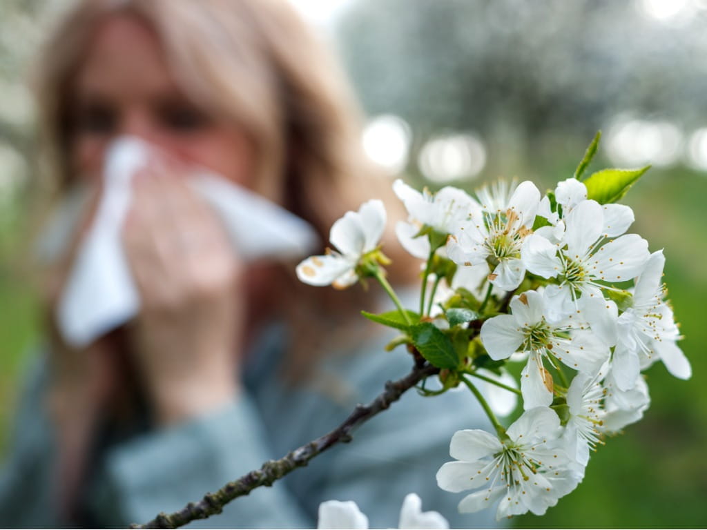 woman blowing her nose behind flowers